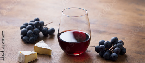 Glass of red wine with fresh grape and cheese on wooden table.