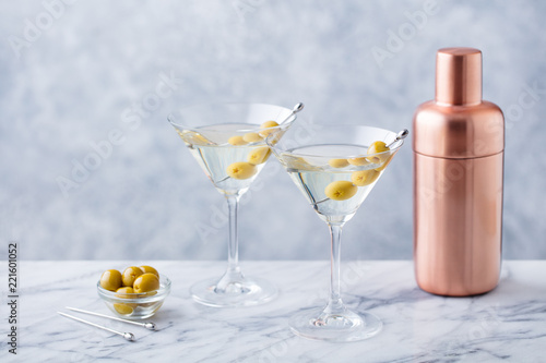 Martini cocktail with olives and bar shaker on marble table background. Copy space.