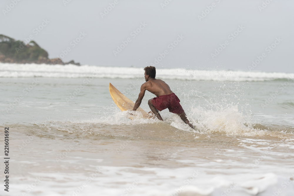 Young dark, handsome, athletic local Native Islander wearing board shorts and showing his six pack abs, rides a wive on his surf board Young dark, handsome, athletic local Native Islander wearing board shorts and showing his six pack abs, rides a wive on his surf board