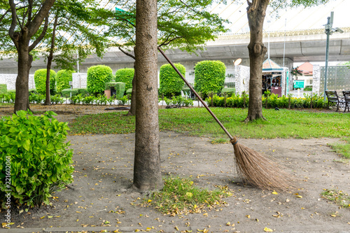 Cleaning in the autumn park - broom and bench with pile of yellow fallen leaves