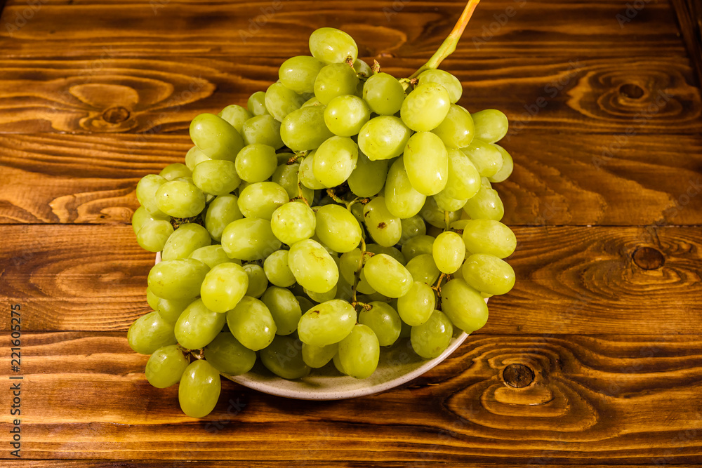 Ceramic plate with green grapes on wooden table Ceramic plate with green grapes on wooden table