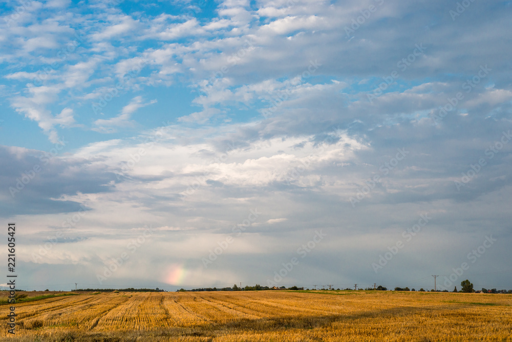 A small piece of rainbow over the field on a hot summer stormy day with a sky in the background. A small piece of rainbow over the field on a hot summer stormy day with a sky in the background.