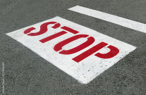 STOP sign with red lettering on white background on street asphalt.  © Noel