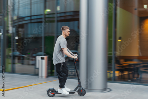 Attractive man riding a kick scooter at cityscape background.