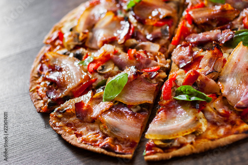 sliced Pizza with Mozzarella cheese, mushrooms, bacon, Tomatoes, pepper, Spices and Fresh Basil. Italian pizza on wooden background.