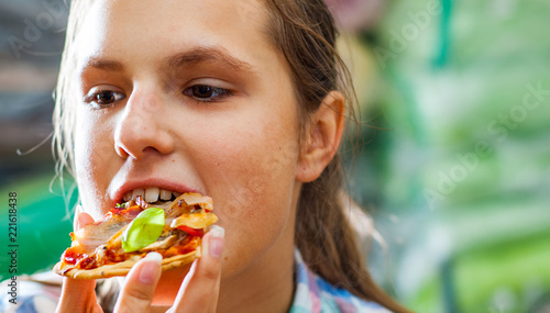 portrait of young teenager brunette girl eating a slice of pizza