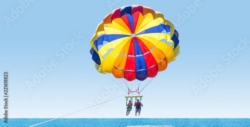 Happy couple Parasailing on Tropical Beach in summer. Couple under parachute hanging mid air. Having fun. Tropical Paradise. Positive human emotions, feelings, family, travel, vacation.