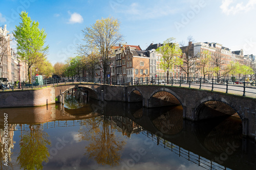 historical houses and arches of bridge over canal with mirror reflections, Amsterdam, Netherlands