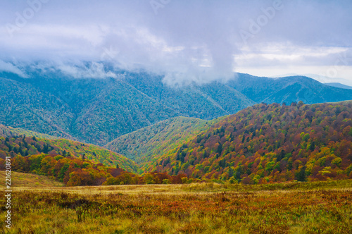 Autumn colors in the background of remote mountains. Clouds fly between the mountains. Autumn mountain landscape