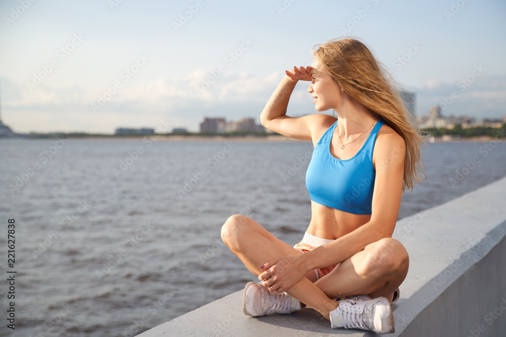 A beautiful sporty girl in an attractive top, shorts and white sneakers looks far away. A beautiful sporty girl in an attractive top, shorts and white sneakers looks far away.