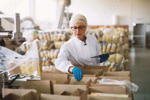 Young female employee in sterile clothes is checking packages ready to be delivered. photo