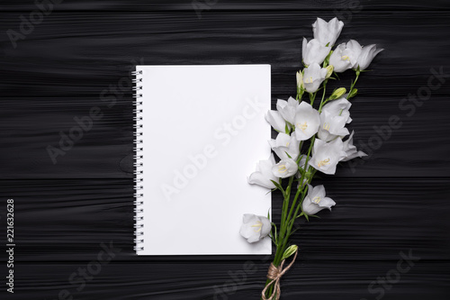 White flowers bells and empty notebook for your text on a black wooden background.