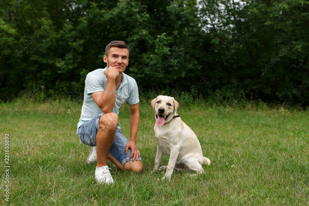 Friendship of man and dog. Happy young man sitting with his friend - dog Labrador