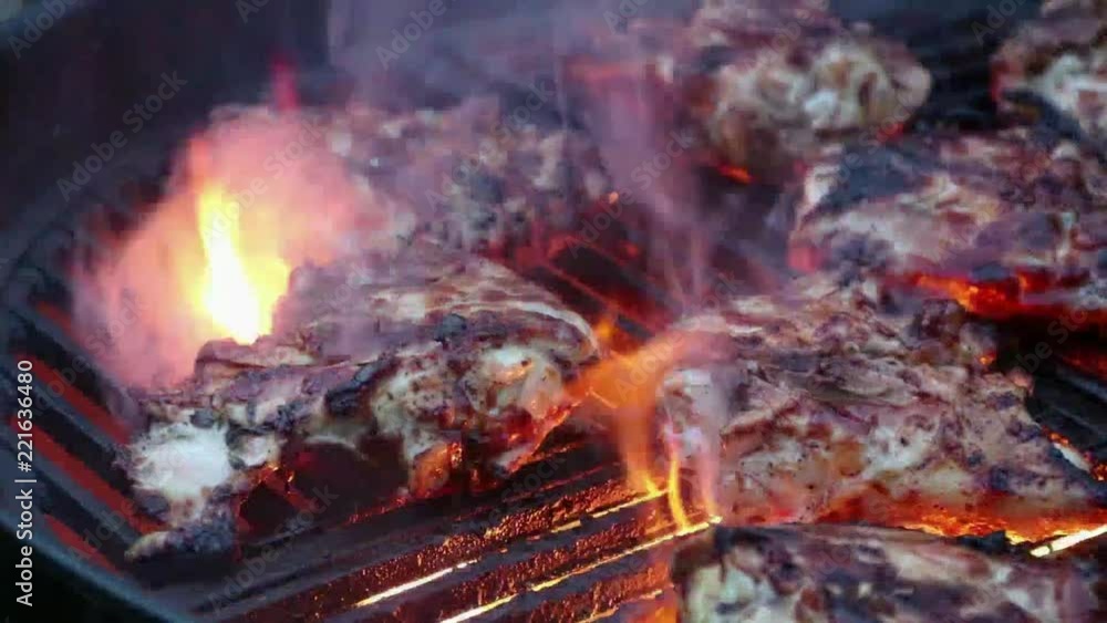 Sizzling chicken thighs on a charcoal grill with flames and smoke rising above the cast iron grates Sizzling chicken thighs on a charcoal grill with flames and smoke rising above the cast iron grates