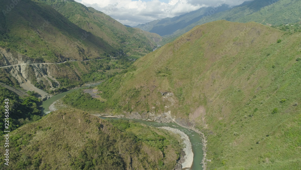 Aerial view of mountain river in the cordillera, road on the slopes, mountains covered forest, trees. Cordillera region. Luzon, Philippines. Mountain landscape in cloudy weather.