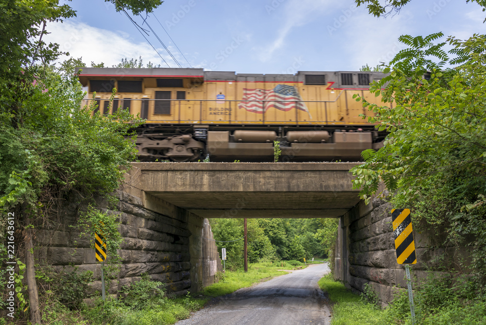 An orange train streaks across a concrete and stone bridge overpass and a lonely country gravel road. An orange train streaks across a concrete and stone bridge overpass and a lonely country gravel road.
