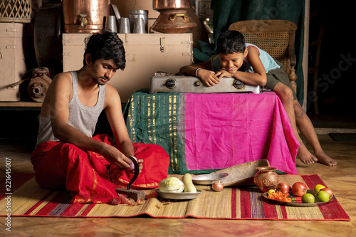 A young man slices vegetables while his friend watches.