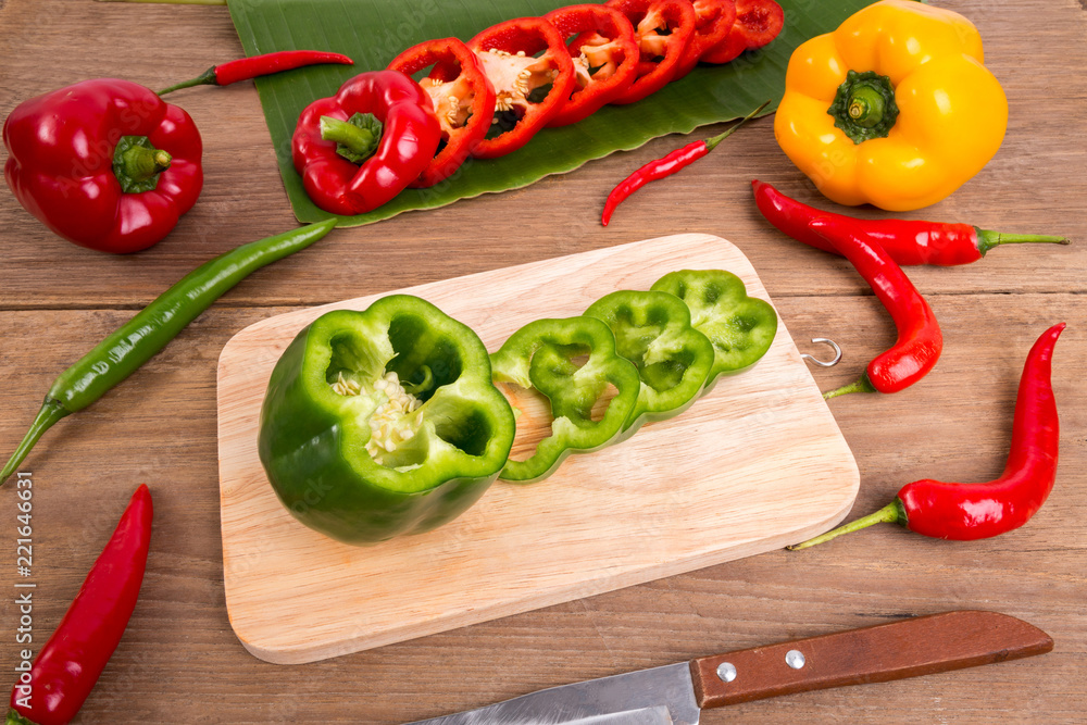Slices of green bell pepper on wood background with wooden board.