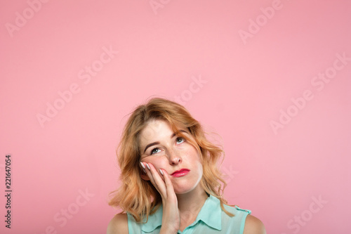 facial expression. low mood and emotion. bored unimpressed disinterested woman looking up. young beautiful blond girl portrait on pink background. photo