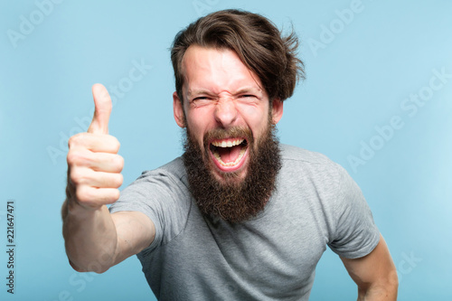 thumb up. good job. like and approval concept. enthusiastic motivated overexcited bearded man showing gesture. cas al hipster guy portrait on blue background. photo