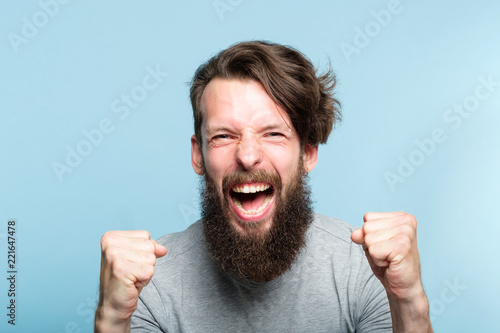 yes success and achievement. happy overexcited enthusiastic exhilarated guy making a win gesture and screaming. thrilled man portrait on blue background.