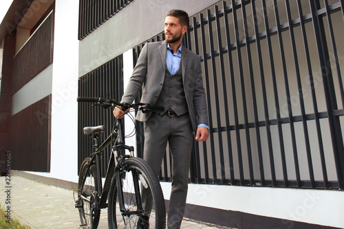 Confident young businessman walking with bicycle on the street in town.