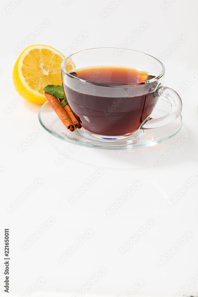 A glass cup with black tea on a saucer with mint, cinnamon, as well as lemon A glass cup with black tea on a saucer with mint, cinnamon, as well as lemon