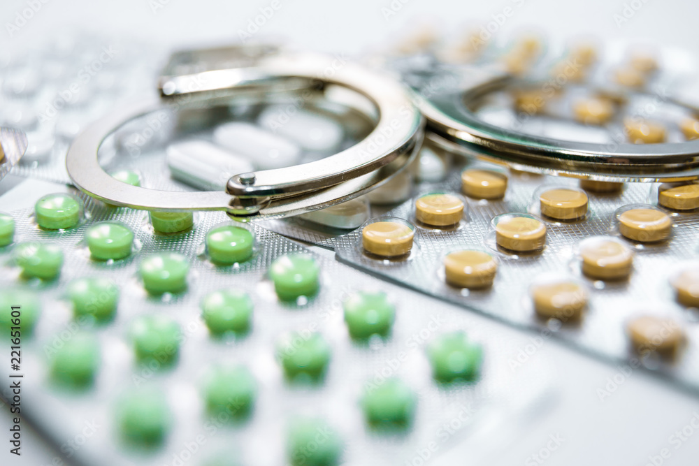 Handcuffs and pills and drugs on white table. Handcuffs and pills and drugs on white table.