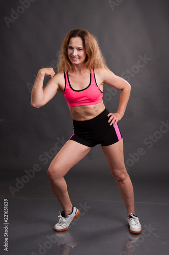Beautiful, athletic, slender woman in a pink shirt and black shorts on a dark background is engaged in fitness, gymnastics