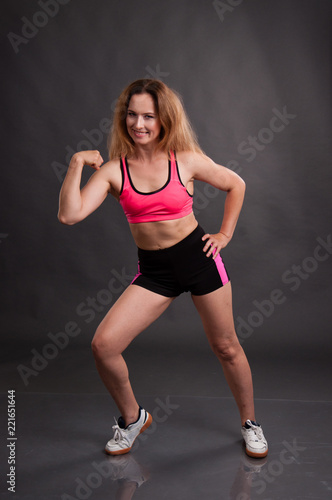 Beautiful, athletic, slender woman in a pink shirt and black shorts on a dark background is engaged in fitness, gymnastics