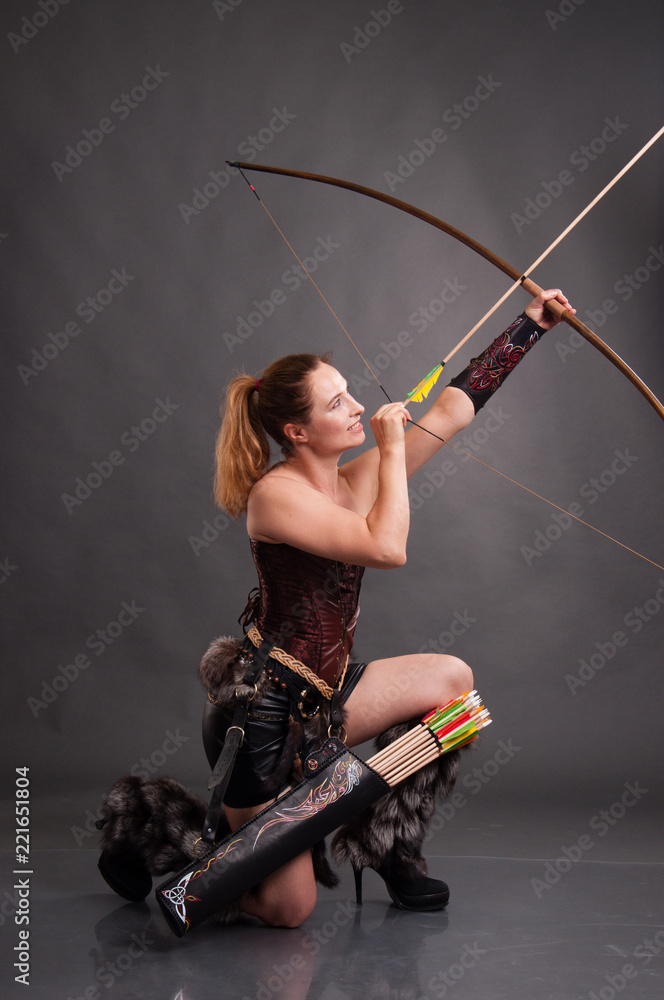 Woman in an amazon suit with a bow on a dark background. The girl shoots from an onion