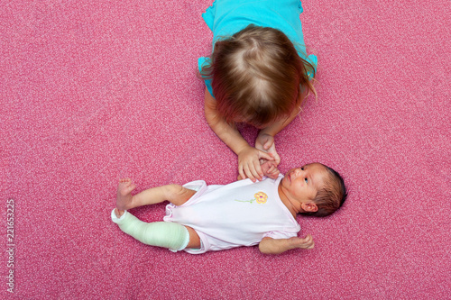 Fotografía Bird Eye View of Older Sister Comforting Newborn Baby Wearing a Cast to Correct