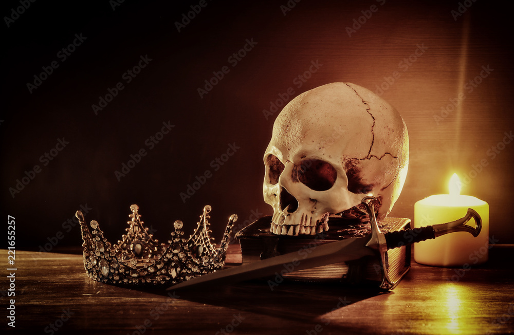 Fototapeta premium Human skull, old book, sword, crown and burning candle over old wooden table and dark background.