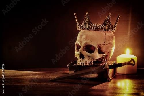 Human skull, old book, sword, crown and burning candle over old wooden table and dark background.