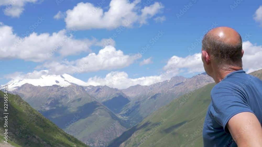 A traveler stands high in the mountains and looks at the top of Elbrus A traveler stands high in the mountains and looks at the top of Elbrus