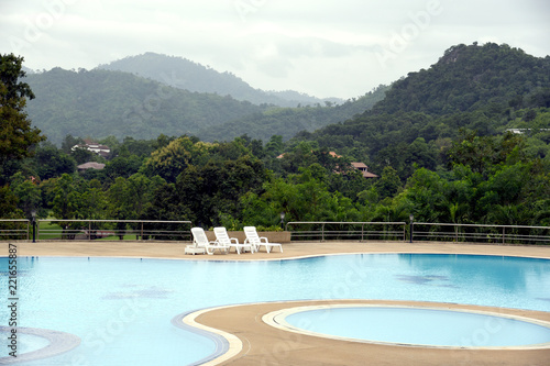 The outdoor swimming pool is in a natural setting with a mountain backdrop.