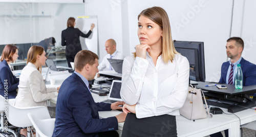 Portrait of unhappy girl in modern open plan office on background with coworkers