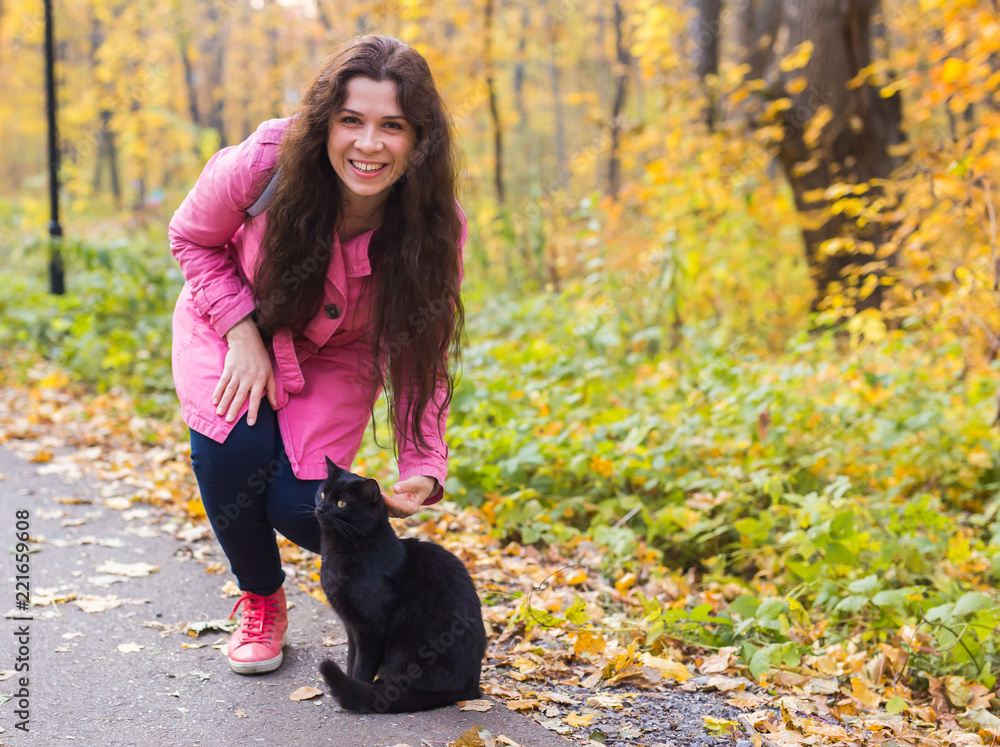 People, pet's owner and season concept - young woman and a black cat in the autumn park People, pet's owner and season concept - young woman and a black cat in the autumn park