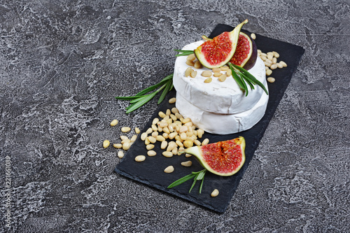 Gourmet appetizer of white brie cheese or camembert with fresh figs, pine nuts and rosemary spice on black slate board