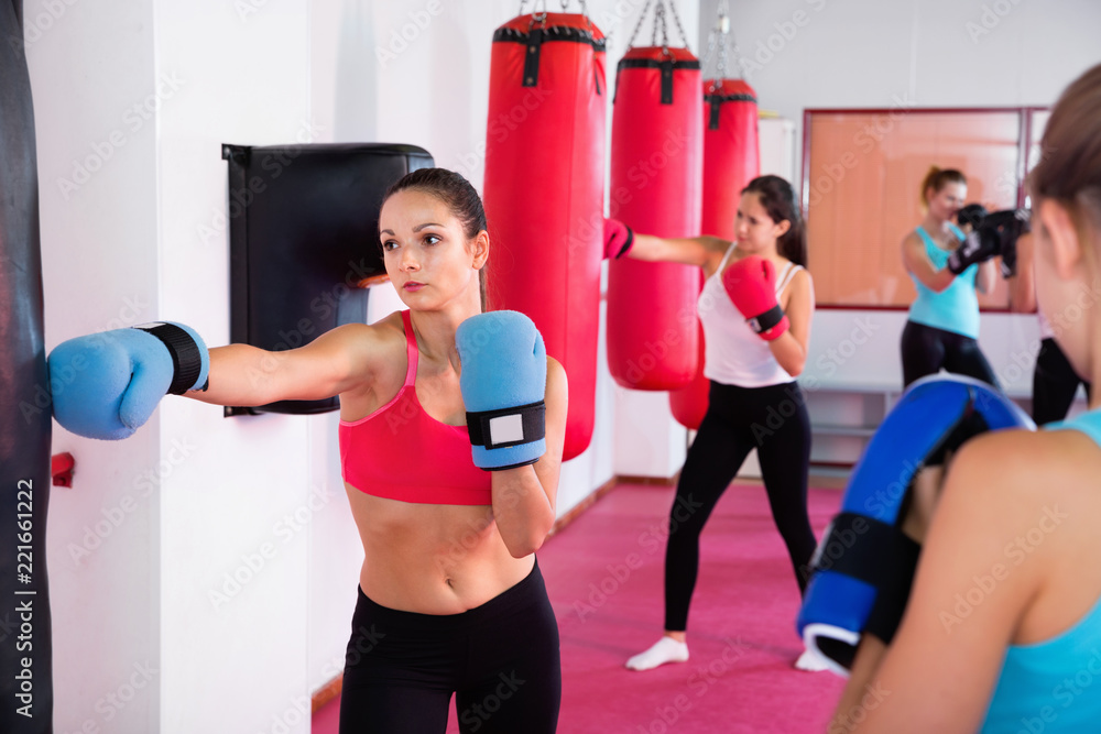 Sporty girl is boxing near punching bag in gym.