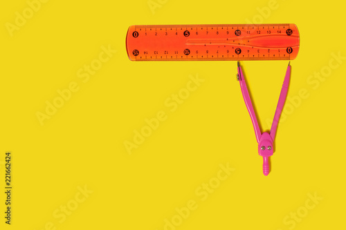 Pair of pink metal compasses lying near an orange ruler on a yellow background. free space for text. concept of school supplies