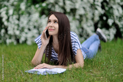 A girl with a phone lying on the grass and calling