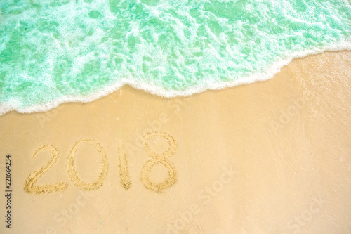 Year 2018 written at the sand beach with sea wave water. wave coming to 2018 concept on the sand beach in the morning.Text 2018 on a beach sand. Concept New Year 2018 is coming soon