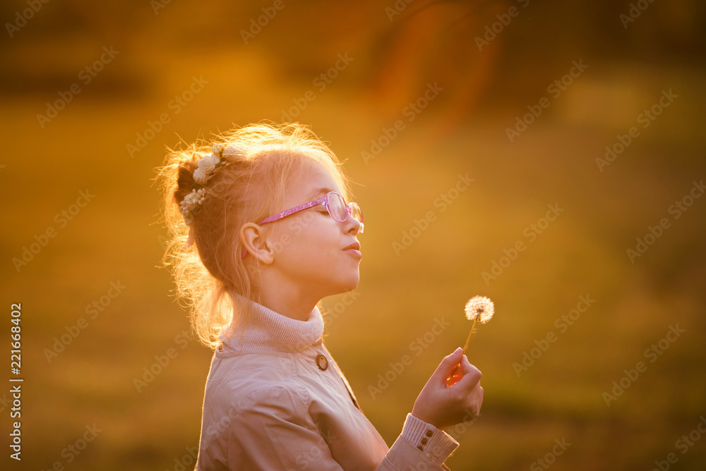 Curly schoolgirl in the glasses and light coat playing with dandelion in the autumn park on the sunset Curly schoolgirl in the glasses and light coat playing with dandelion in the autumn park on the sunset