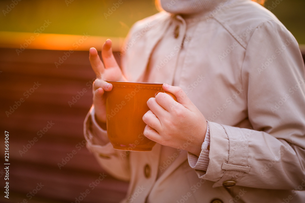 The brown hot cup in hand of the child in the autumn park The brown hot cup in hand of the child in the autumn park