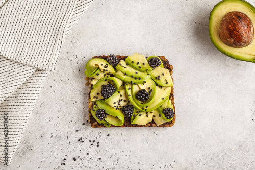 Avocado toast on a healthy sesame bread with blackberry and sesame seeds, top view. Healthy vegan food concept.