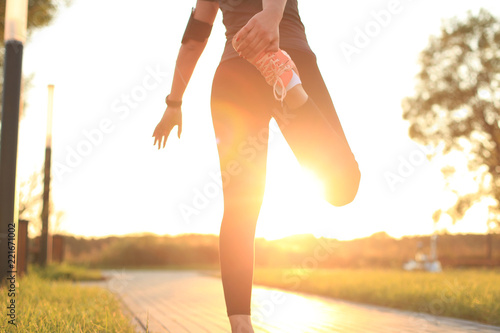 Young attractive sporty fitness woman runner warming up before run at sunset or sunrise on city.
