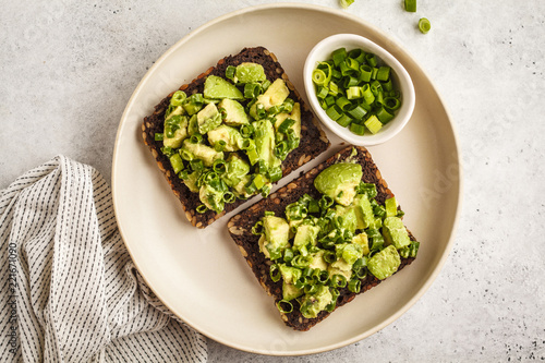 Avocado toast with whole wheat bread, avocado and green onion on white plate, top view.