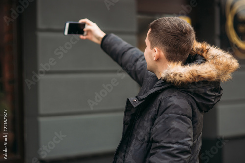 Man in a gray jacket is standing outside and using a phone