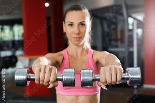 Athletic beautiful woman wearing pink and black sportswear doing exercise using dumbbells close up in a gym. Strength and motivation concept